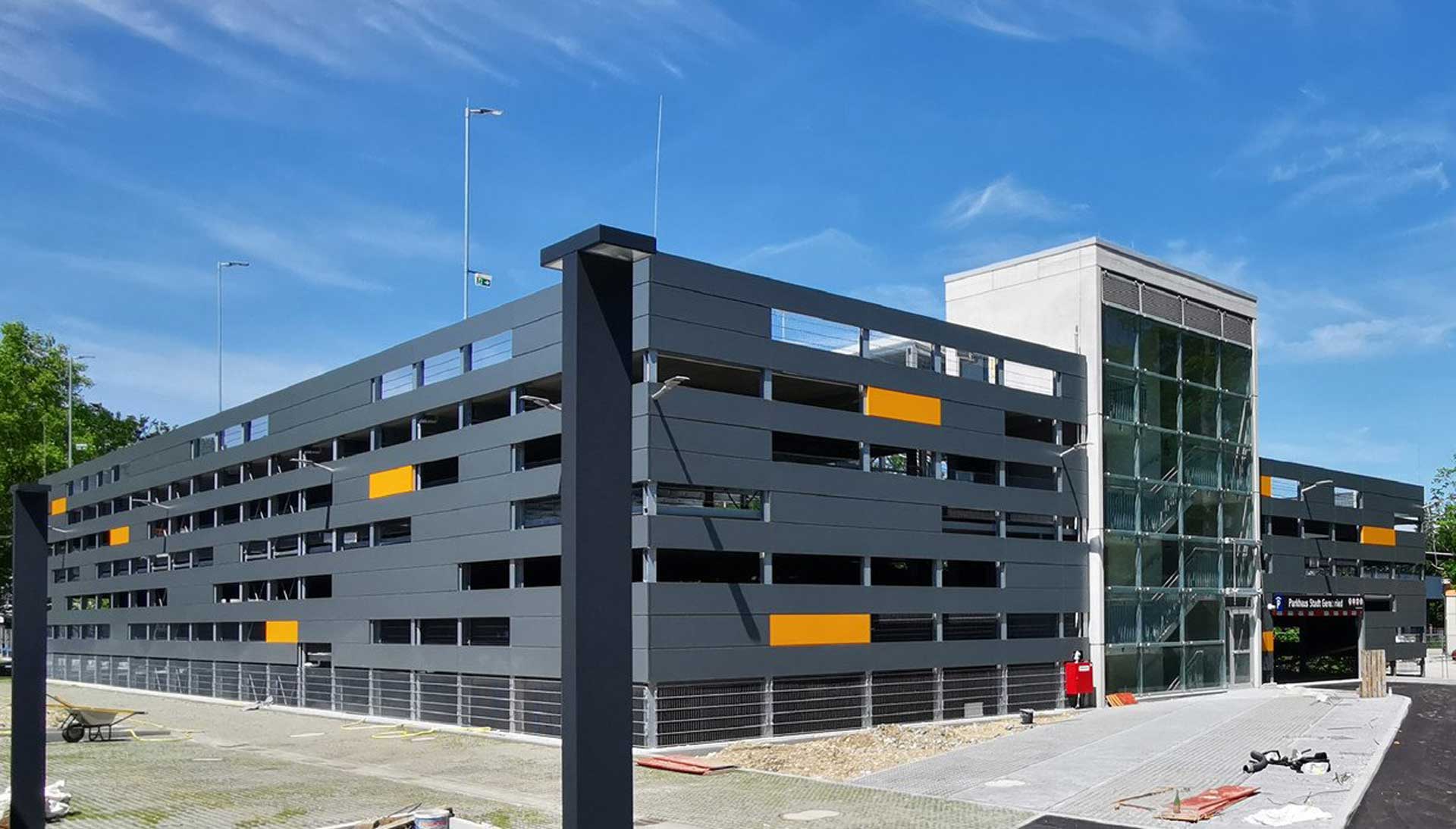 Modernes Parkhaus mit grauer Fassade, orangefarbenen Akzenten und verglastem Treppenhaus.